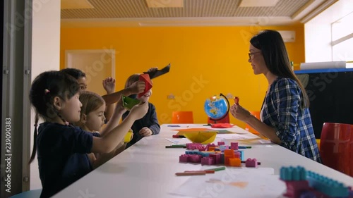 Joyful carefree multi ethnic diverse children playing with handmade origami toys at craft lesson. Happy kindergarten teacher and little students having fun in preschool class. photo