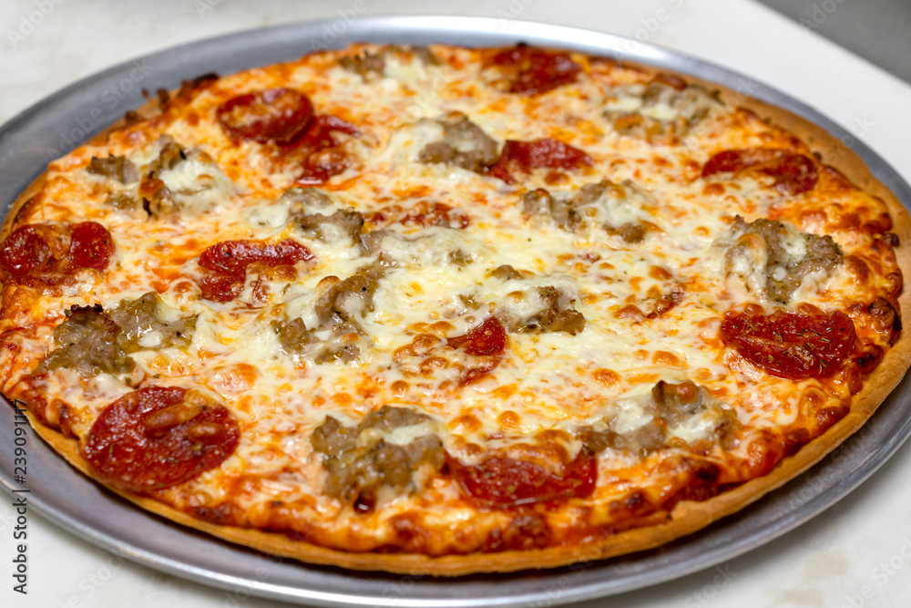 Sausage and pepperoni pizza fresh out of the oven. Not cut. Whole pizza on pan. Prepared in a restaurant. Sausage and pepperoni pizza fresh out of the oven. Not cut. Whole pizza on pan. Prepared in a restaurant.