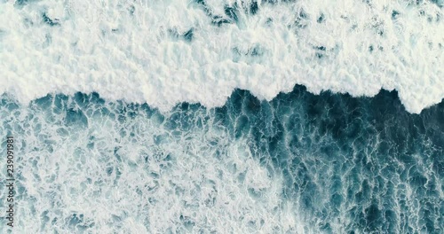 Aerial headover drone footage of huge waves crashing on dark sand of the coast 4K