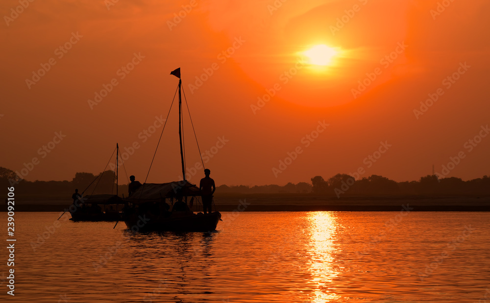 Beautiful orange colored sunset on a Ganges river with a silhouette of a boat and people.