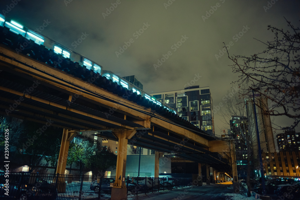 Elevated subway train on a vintage urban city railway bridge with an alley during the winter at night