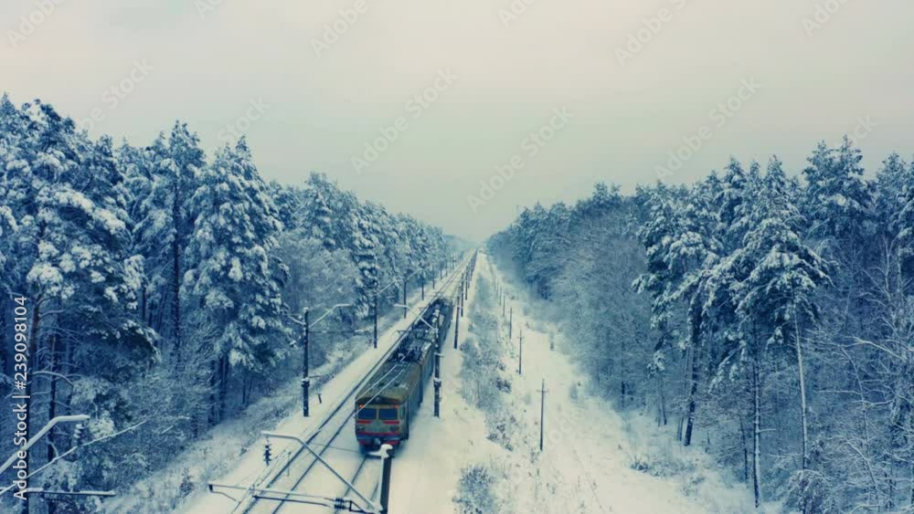 Aerial following shot of suburban train rides through the winter snowy forest 