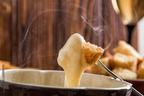Close up, macro. Traditional french cheese fondue. Crouton dipped into stemy-hot cheese fondue on a long-stemmed fork. Copy space. photo