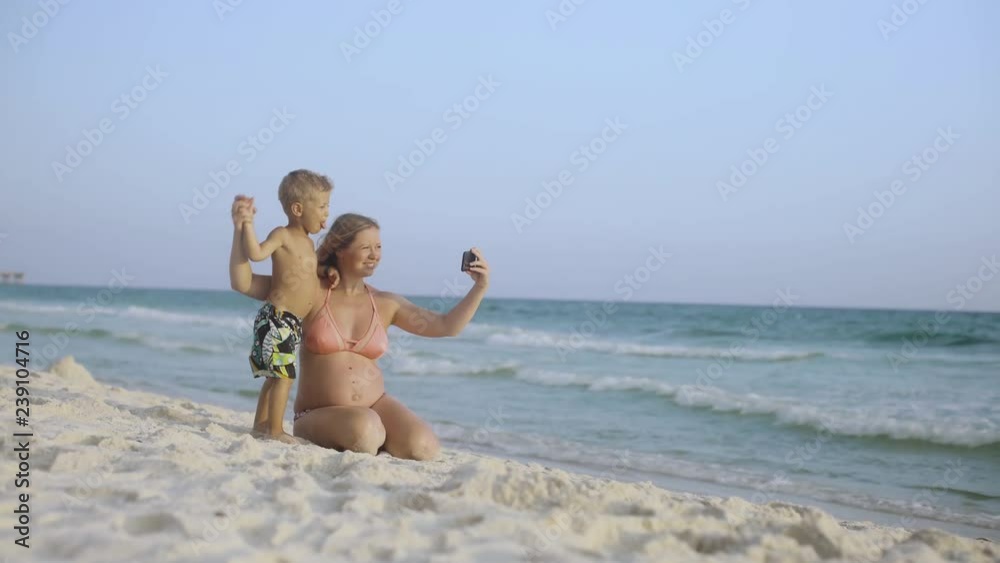 Young beautiful positive mother is sitting with her little son and making a selfie on a smartphone on the beach 4k Young beautiful positive mother is sitting with her little son and making a selfie on a smartphone on the beach 4k