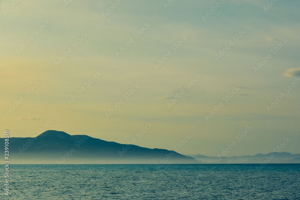 beautiful line of sea and blue-yellow sky. majestic mountains in the fog beautiful line of sea and blue-yellow sky. majestic mountains in the fog
