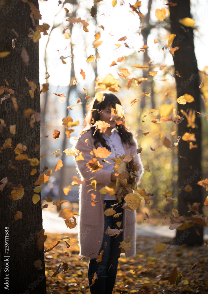 The girl stands under the autumn falling leaves in the park