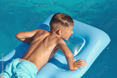  Caucasian boy  is  laying on blue  inflatable mattress at hotel swimming pool. He is enjoying his summer vacations.