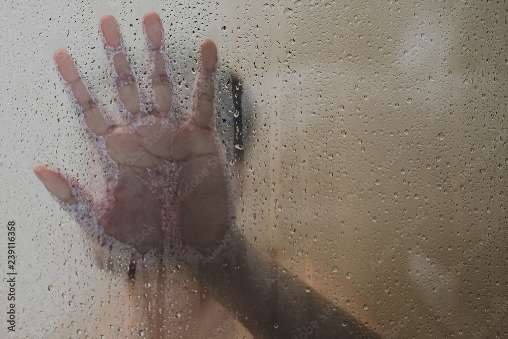 man and hand standing in the shower room behind the wet glass. Artistic darkness and texture man and hand standing in the shower room behind the wet glass. Artistic darkness and texture