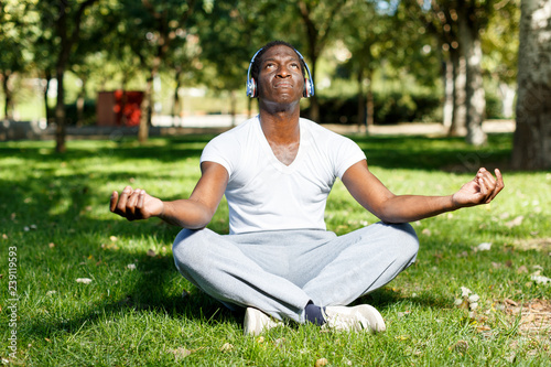 Athletic african american in headphones sitting before training in park