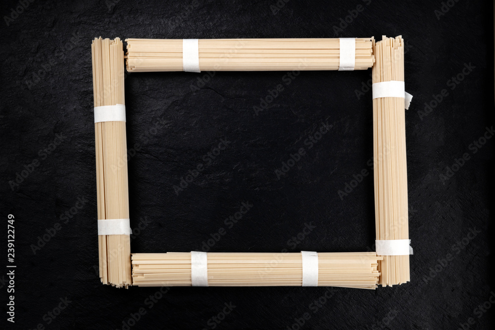 Obraz premium A photo of individually wrapped portions of udon noodles, shot from above, forming a frame on a black background with a place for text