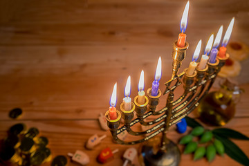 Jewish holiday hanukkah celebration with menorah (traditional candelabra), wooden dreidels (spinning top), donut, olive oil and chocolate coins on wooden table.