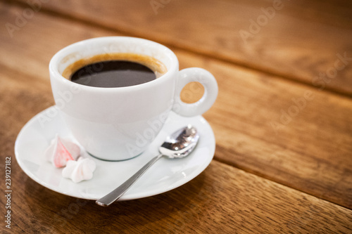 a cup of coffee bize on a saucer and a spoon stands on a wooden table. aromatic hot fresh coffee. wooden vintage table background with diagonal lines. for design and decor. selective focus