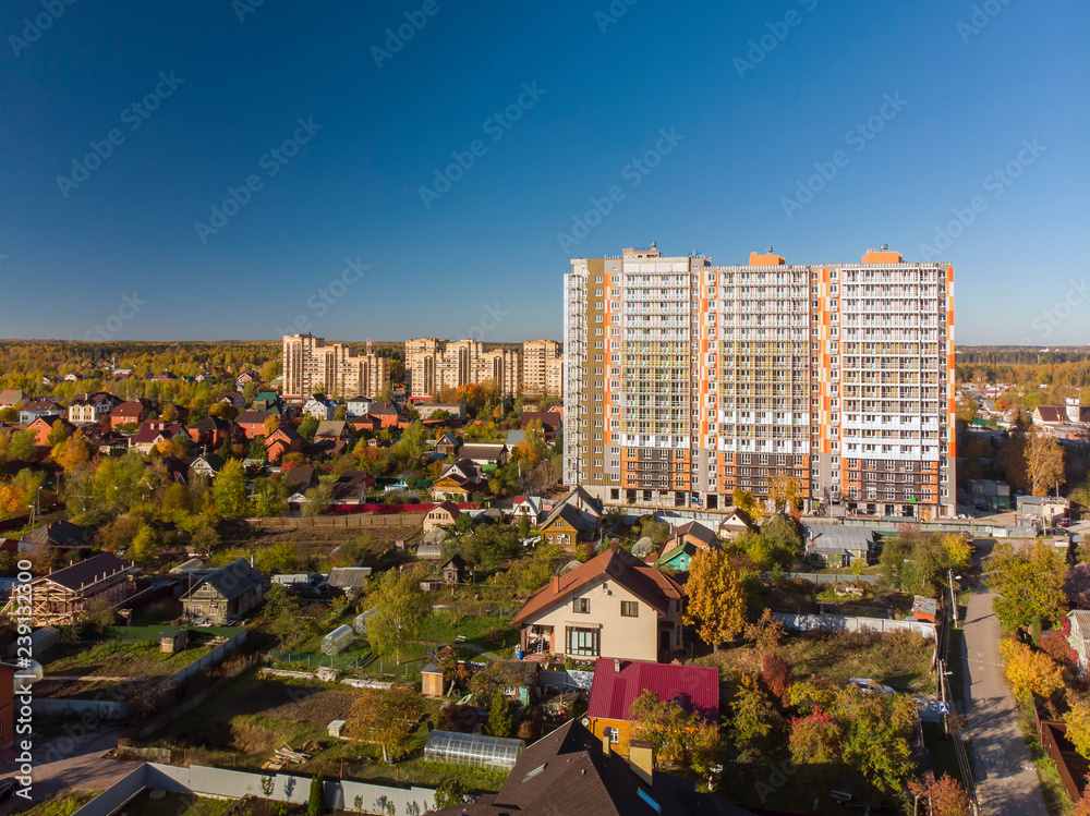 Naklejka premium High-rise residential building under construction among private houses in Russia