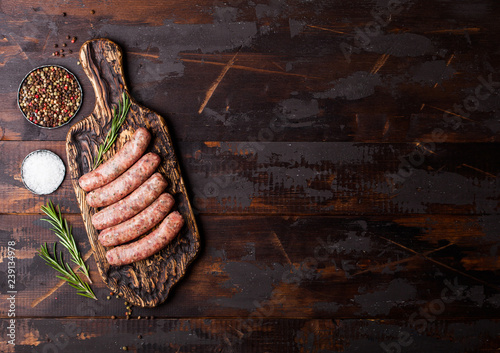 Canvas Print Raw beef and pork sausage on vintage chopping board with salt and pepper on dark wooden background