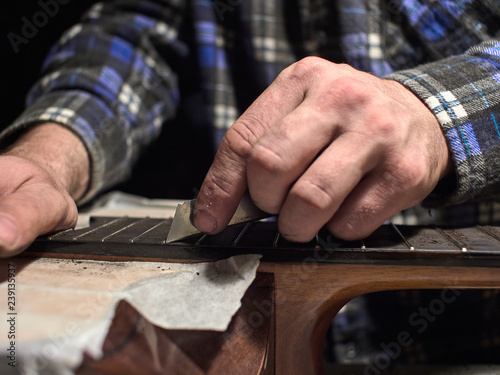 Installation frets on the neck of the guitar. The specialist cycles the fingerboard.