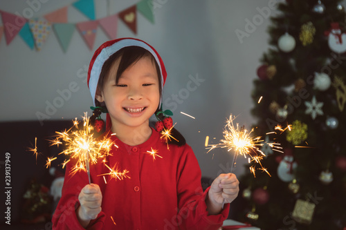 Asian girl playing sparkler at party with decorating gift box and christmas tree in living room at home.Smiling face and happy to celebrate festivel new year holiday with family.
