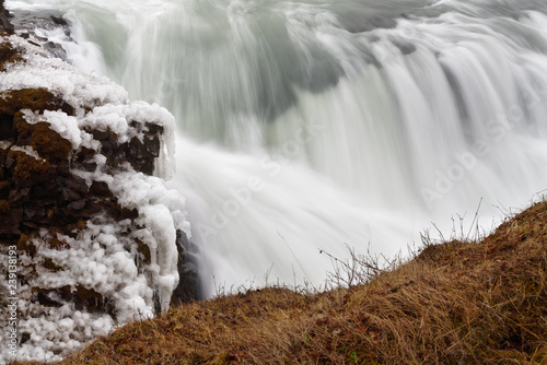 Detail view of flowing water of a huge waterfall in winter, icicles on the rocks next to the cascade, long time exposure, flow structure - Location: Iceland, Golden circle, Gullfoss