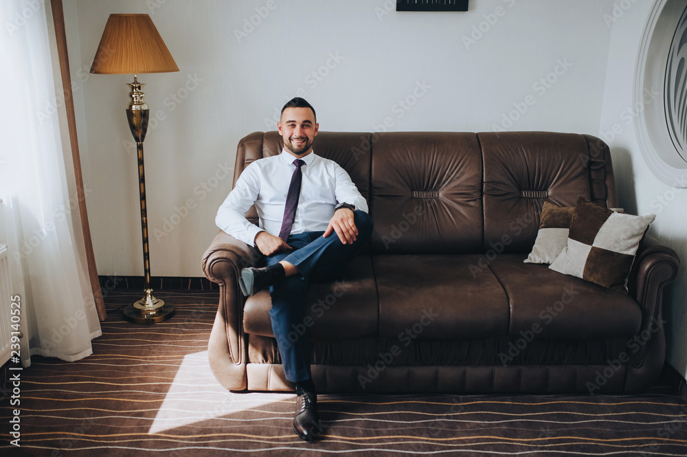 Handsome groom with a beard sitting on the sofa. Wedding interior. Fees groom in the room. Wedding concept. Wedding photography.