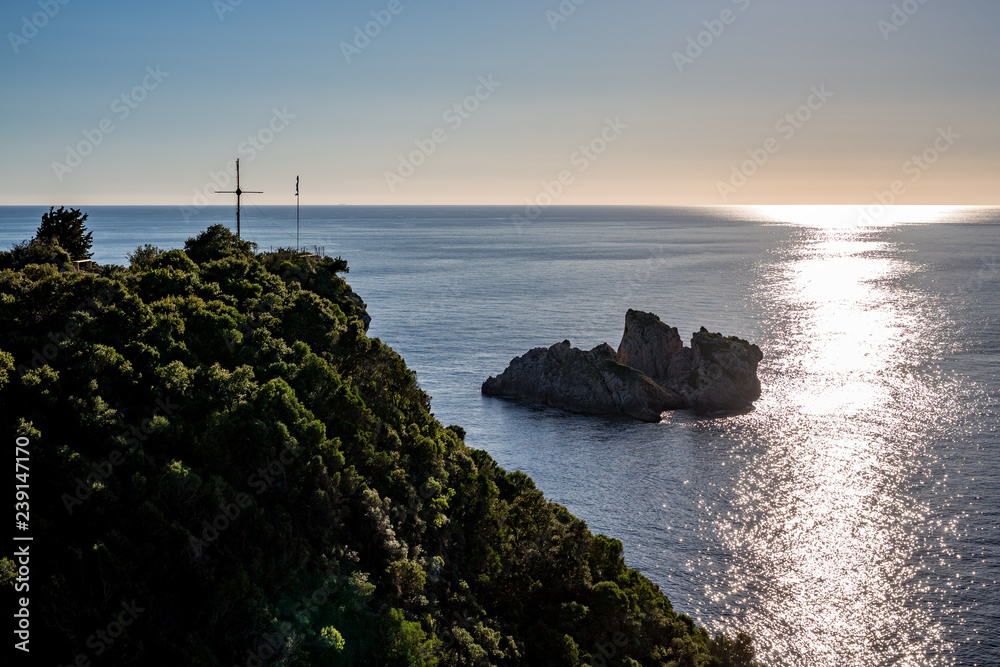 Picturesque landscape view from Cofru, Greece, shiny sun path, small island and big Christian cross on green hill above the Ionian Sea in a clear blue sky spring day