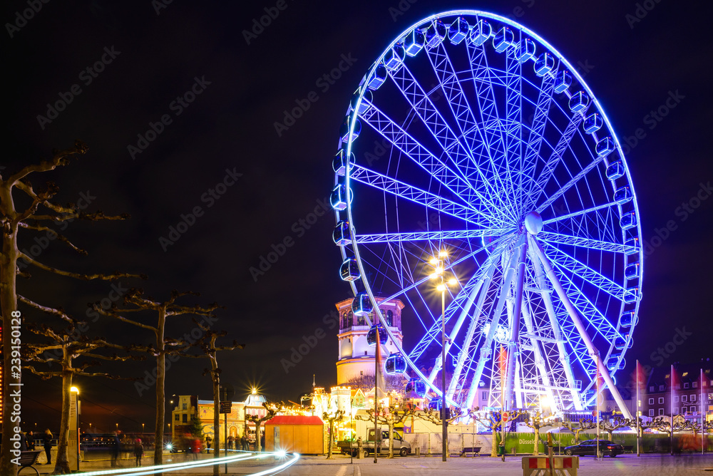 Night scenery on promenade and walkway along riverside of Rhine river and background of Ferris wheel of Christmas market festival, Weihnachtsmarkt, in Düsseldorf, Germany.