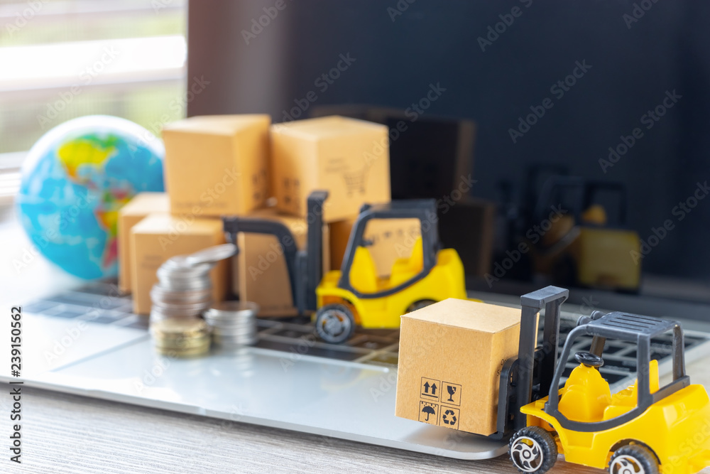 Mini forklift truck load cardboard box, stack of coins and pile of boxes on laptop keyboard with globe near by. Logistics and transportation management ideas and Industry business commercial concept.