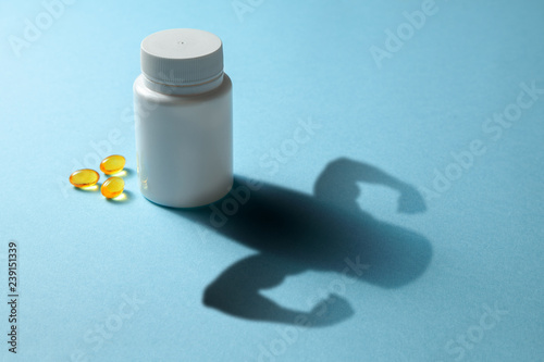 The concept of fish oil gives strength. Bottle with pills and shadow in the shape of the arms with biceps muscles. Yellow fish oil capsules photo