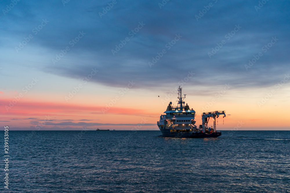 Buoy-Laying Vessel departing from Dun Laoghaire harbor at sunrise in Dublin, Ireland. Seascape with an advanced multifunctional ship in the Irish Sea at dusk.