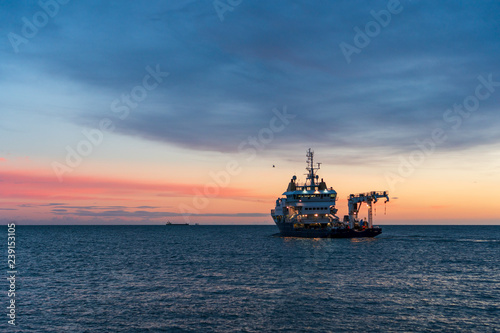 Buoy-Laying Vessel departing from Dun Laoghaire harbor at sunrise in Dublin, Ireland. Seascape with an advanced multifunctional ship in the Irish Sea at dusk.