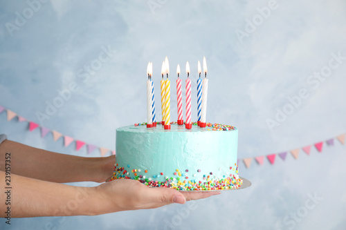 Woman holding fresh delicious birthday cake with candles on color background