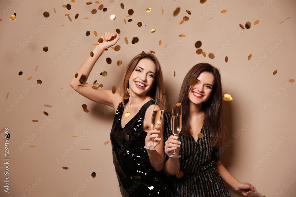 Plakat Beautiful women with glasses of champagne and confetti on color background