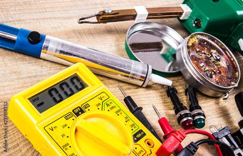 Electrical tester and other tools of electrician on a wooden background.