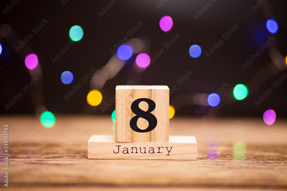 Naklejka premium January 8th. Day 8 of January set on wooden calendar on dark background with garland bokeh. Winter time. Holiday Composition