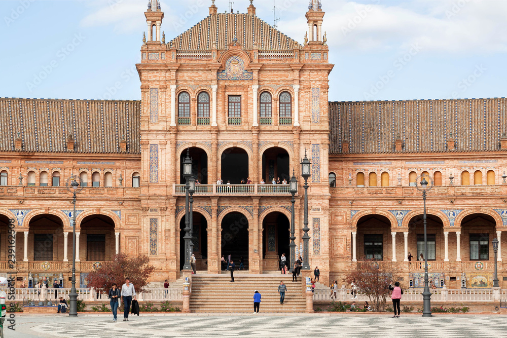 People walking around historical palace and stone bridge on Plaza de Espana, example of architecture of Andalusia