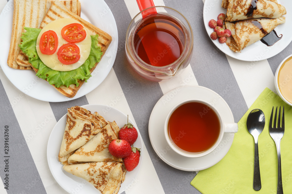 Fresh, tasty breakfast with a sandwich, pancakes and tea on a light background.