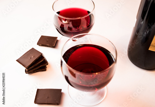 Two glasses with red wine, pieces of dark chocolate and a bottle of wine isolated on a white background.