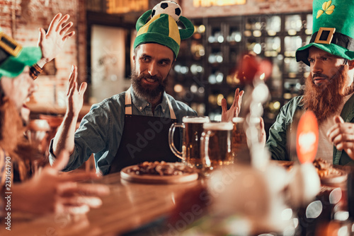 Handsome bearded man in apron chatting with friends at pub