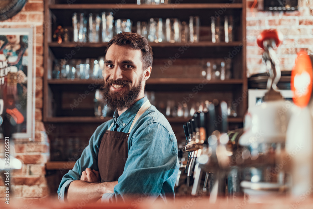 Cheerful barman with crossed arms standing at the bar counter Cheerful barman with crossed arms standing at the bar counter