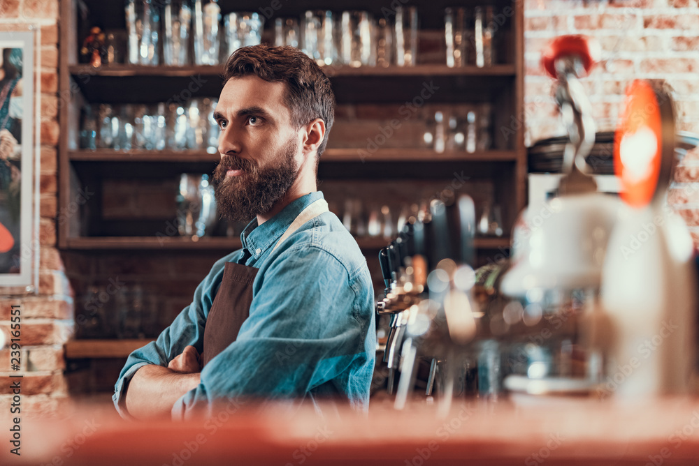 Handsome bartender with crossed arms standing at the bar counter