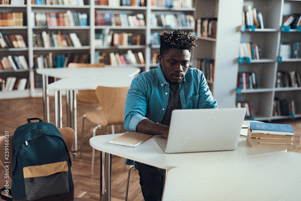 Calm student working on his laptop while sitting alone Calm student working on his laptop while sitting alone