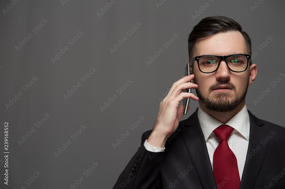 Close-up - Serious young businessman in formal suit talking to someone on smartphone on gray background. Place for text Close-up - Serious young businessman in formal suit talking to someone on smartphone on gray background. Place for text