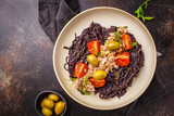 Black rice pasta with tuna, tomatoes and olives in a white plate, top view.