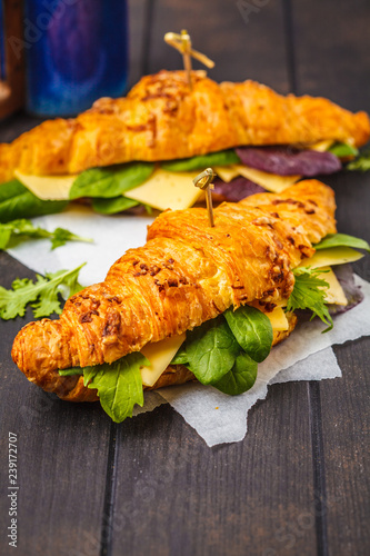 Croissants with cheese and salad on dark wooden background.