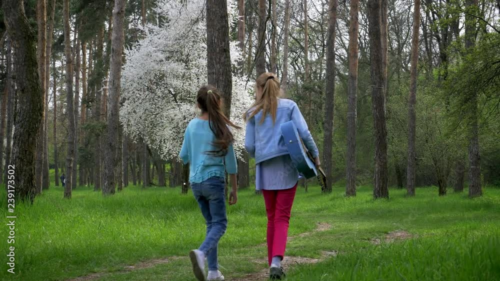children walk in the Park. Little girlfriends are walking in nature with acoustic guitar . beautiful forest path, juvenile girl outgoing in the distance. emotions and joy children walk in the Park. Little girlfriends are walking in nature with acoustic guitar . beautiful forest path, juvenile girl outgoing in the distance. emotions and joy