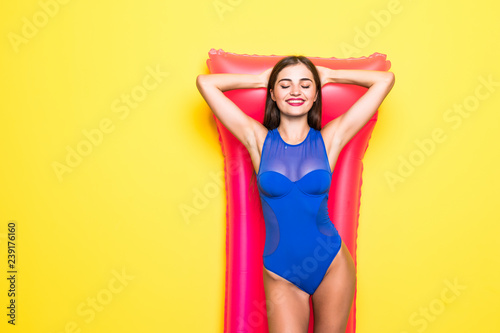 Young sexy woman posing with pink inflatable mattress, isolated on yellow background © dianagrytsku