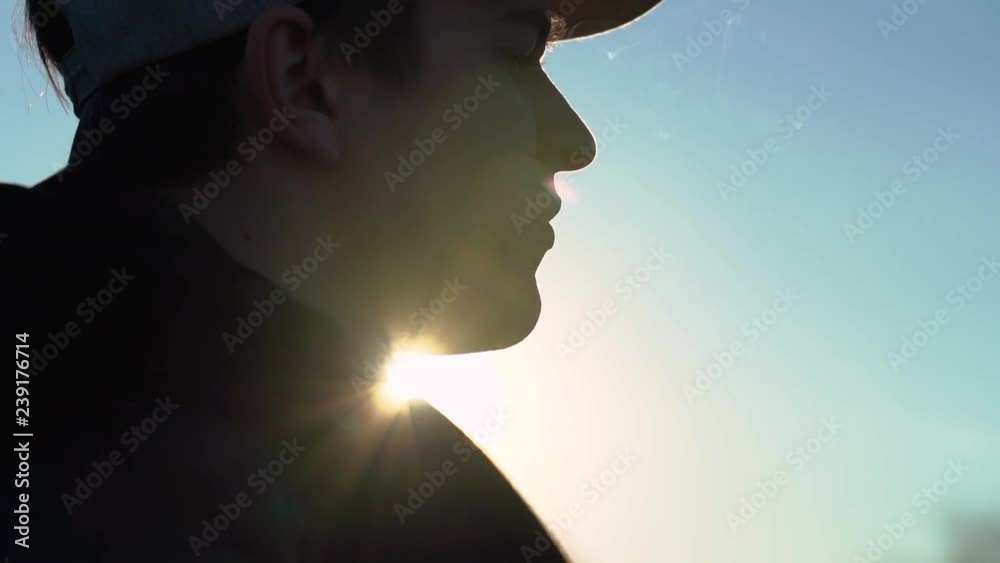 A young guy in a cap smokes an electronic cigarette at sunset, smoke burns in the sun, slow motion video A young guy in a cap smokes an electronic cigarette at sunset, smoke burns in the sun, slow motion video