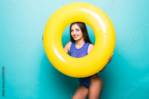 Portrait of a laughing girl dressed in blue swimsuit looking through inflatable ring isolated over blue background