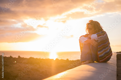 Beautiful curly woman sitting on a wall and enjoy the sunset time feeling the freedom sensation on her skin and feed with nice thoughts her mind - mexican casual style and hippy concept © simona