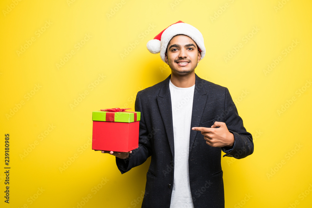 Smiling indian man in Santa Hat Pointing at Big Gift Box isolated on yellow background