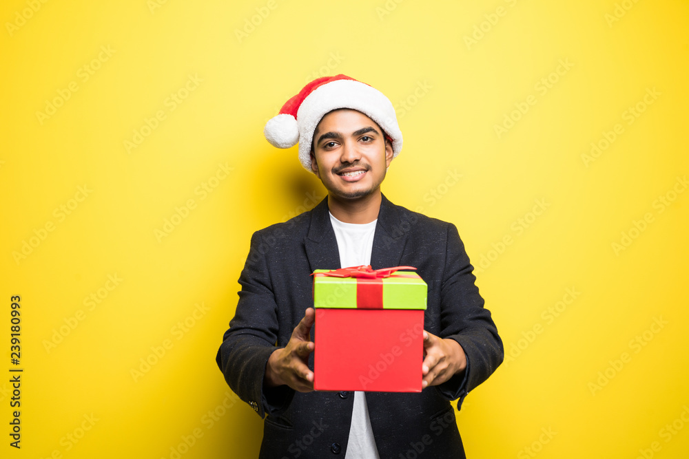 Portrait of happy indian man wearing santa hat and holding gift box isolated on yellow background Portrait of happy indian man wearing santa hat and holding gift box isolated on yellow background