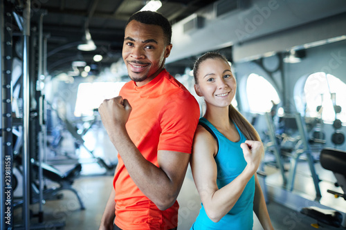 Young successful sports coaches in activewear showing gesture of strength while looking at you